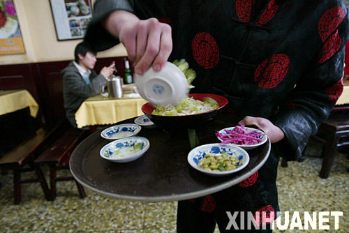 北京京味精小吃店身着传统服装的店小二将菜码倒入盛面的大碗，现场为顾客调制炸酱面（11月4日摄）。